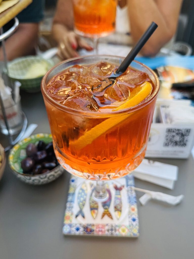 Aperol Spritz in a rocks glass with an orange slice, olives on the table