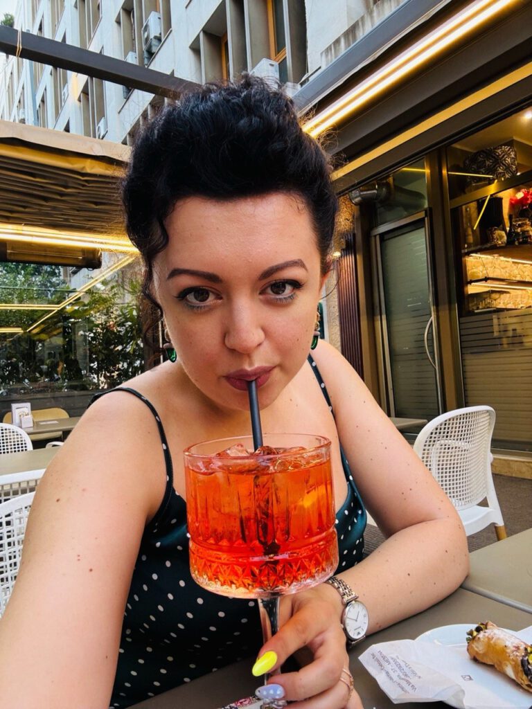 Woman sipping an Aperol Spritz through a straw at an outdoor café