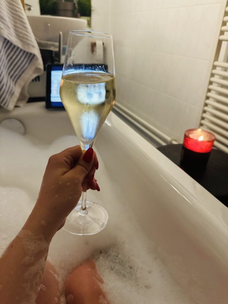 Hand holding a glass of champagne in a candlelit bubble bath